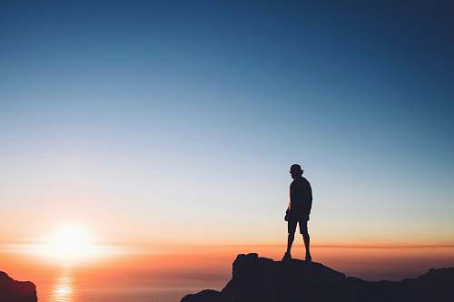 south africa silhouette photo of man standing on peak front of the sea table mountain (nature reserve)